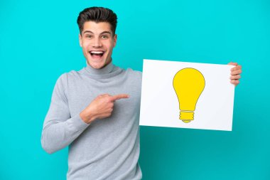 Genç, beyaz bir adam mavi bir bakkal sahasında izole edilmiş. Elinde ampul simgesi olan bir pankart var.