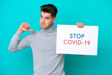 Genç beyaz adam mavi bakkalda izole edilmiş. Elinde yazılı bir levha var. Covid 19 'u gururla durdur.