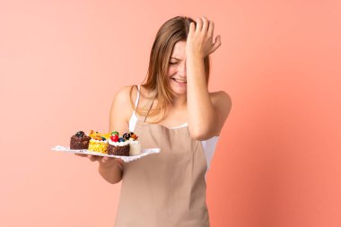 Pastacı Ukraynalı şef pembe arka planda izole edilmiş bir kek tutuyor. Kafası karışık bir yüz ifadesi var.