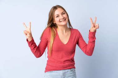 Mavi arka planda izole edilmiş genç Ukraynalı kız iki eliyle zafer işareti gösteriyor.