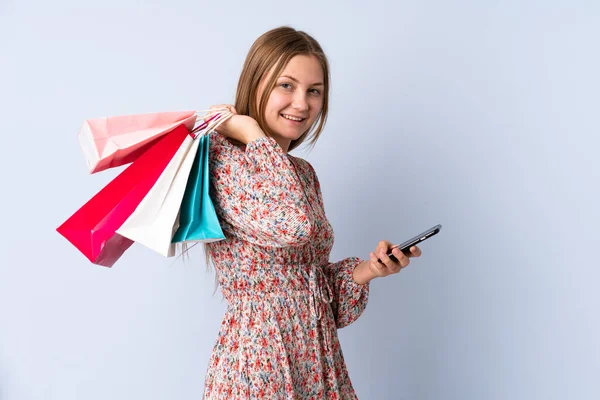 乌克兰少女孤身一人 蓝色背景 提着购物袋 用手机给朋友留言 — 图库照片