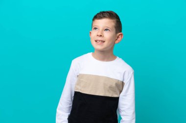 Küçük çocuk mavi arka planda izole edilmiş, yukarı bakarken bir fikir düşünüyor.