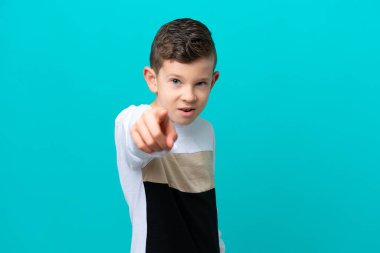 Küçük çocuk mavi arka planda izole edilmiş hayal kırıklığına uğramış ve ön tarafı işaret ediyor.