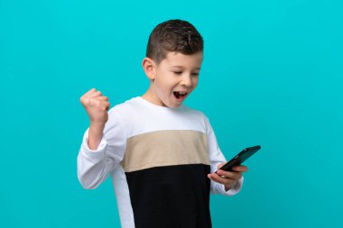 Küçük çocuk mavi arka planda izole edilmiş ve telefon zafer pozisyonunda.