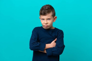 Küçük çocuk mutsuz bir ifadeyle mavi arka planda izole edilmiş.