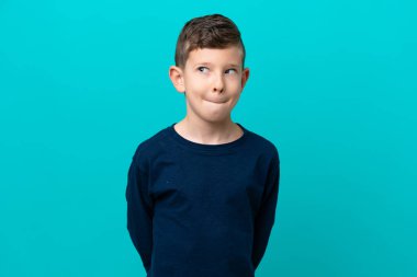 Küçük çocuk mavi arka planda izole edilmiş, yukarı bakarken şüpheleri var.