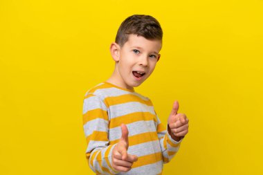 Sarı arka planda izole edilmiş küçük beyaz çocuk önü işaret ediyor ve gülümsüyor.