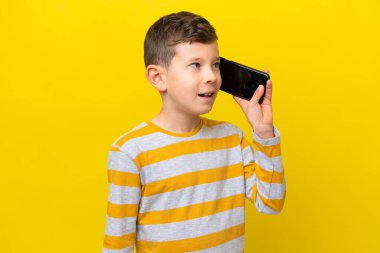 Sarı arka planda izole edilmiş küçük beyaz çocuk cep telefonuyla sohbet ediyor.