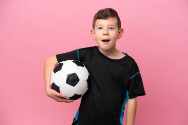 Küçük beyaz futbolcu çocuk, pembe arka planda yalıtılmış, şaşırmış bir yüz ifadesi var.