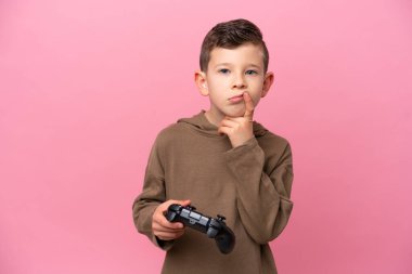 Pembe arka planda izole edilmiş bir bilgisayar oyunu kontrolörüyle oynayan beyaz bir çocuk.