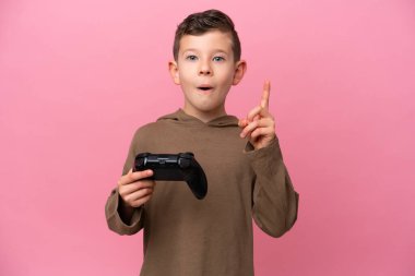 Pembe arka planda izole edilmiş bir bilgisayar oyunu kontrolörüyle oynayan küçük beyaz çocuk çözümü fark etmek için parmağını kaldırıyor.