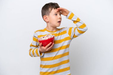 Beyaz arka planda yalıtılmış mısır gevreği kasesi tutan küçük beyaz çocuk yan tarafa bakarken sürpriz jest yapıyor.