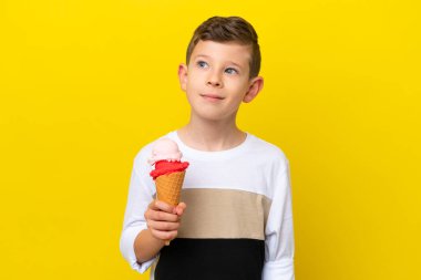 Kornet dondurmalı küçük beyaz çocuk sarı arka planda izole edilmiş ve yukarı bakıyor.