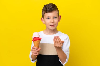 Kornet dondurması olan beyaz bir çocuk sarı arka planda izole edilmiş bir şekilde benimle gelmesi için davet ediyor. Gelmene sevindim.