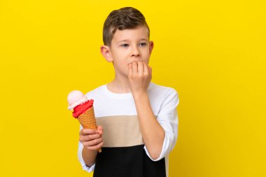 Kornet dondurması olan küçük beyaz bir çocuk sarı arka planda izole edilmiş kuşkuları var.