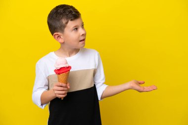 Kornet dondurması olan beyaz bir çocuk sarı arka planda, şaşırmış bir ifadeyle yan yana bakarken.