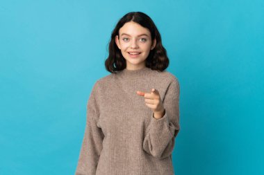 Genç Ukraynalı kız mavi arka planda izole edilmiş şaşırmış ve ön tarafı işaret ediyor.