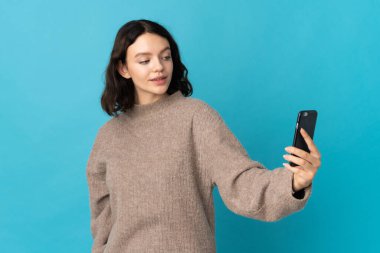 Mavi arka planda izole edilmiş genç Ukraynalı kız selfie çekiyor.