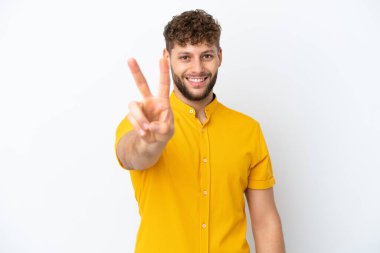 Beyaz arka planda izole edilmiş yakışıklı beyaz adam gülümsüyor ve zafer işareti gösteriyor.