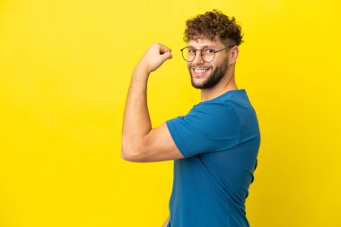 Sarı arka planda izole edilmiş yakışıklı beyaz adam güçlü bir jest yapıyor.
