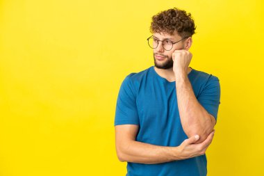 Sarı arka planda izole edilmiş, yorgun ve sıkılmış bir ifadeyle genç, beyaz bir adam.