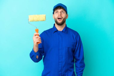 Kafkasyalı ressam mavi arka planda izole edilmiş yukarı bakıyor ve şaşırmış bir ifadeyle