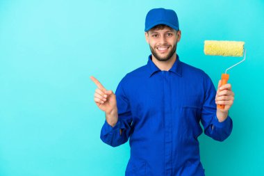 Kafkasyalı ressam, mavi arka planda izole edilmiş bir şekilde bir ürün sunmak için kenarı işaret ediyor.
