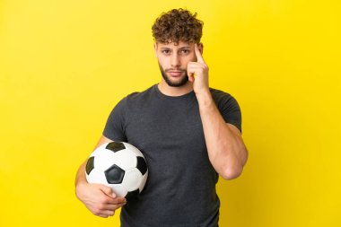 Yakışıklı genç futbolcu sarı arka planda izole edilmiş bir fikir düşünüyor.
