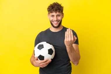 Yakışıklı genç futbolcu, sarı arka planda izole edilmiş bir şekilde el ele gelmeye davet ediliyor. Gelmene sevindim.