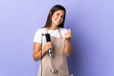 Mor arka planda izole edilmiş el blenderi kullanan Brezilyalı kadın para hareketi yapıyor