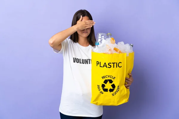 若いブラジル人女性は手で目を覆う紫色の背景に隔離されたリサイクルするためにペットボトルでいっぱいの袋を持っています 何か見たくない — ストック写真