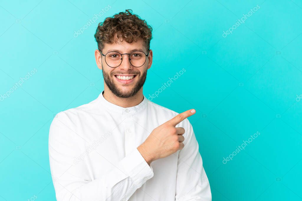 Young handsome caucasian man isolated on blue background With glasses and pointing side