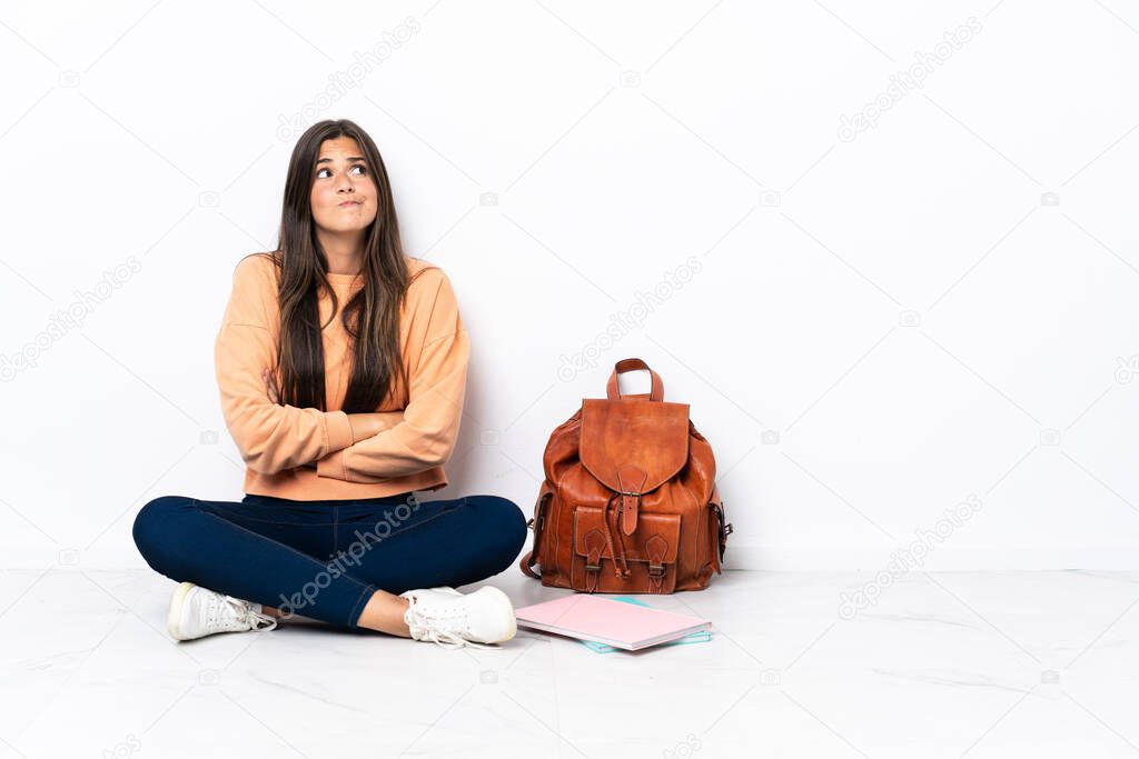 Young student brazilian woman sitting on the floor making doubts gesture while lifting the shoulders