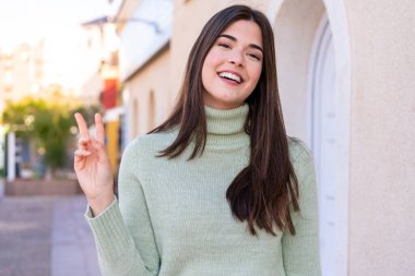 Dışarıdaki Brezilyalı genç kadın gülümsüyor ve zafer işareti gösteriyor.