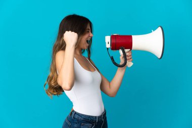 Mavi arka planda izole edilmiş genç beyaz bir kadın megafondan bir şey duyurmak için bağırıyor.