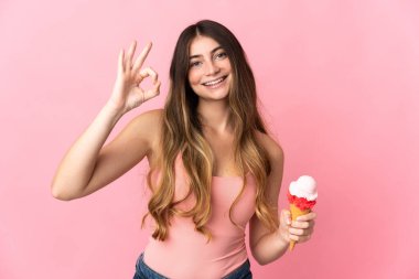 Kornet dondurması olan beyaz bir kadın pembe arka planda izole edilmiş. Parmaklarıyla işaret veriyor.