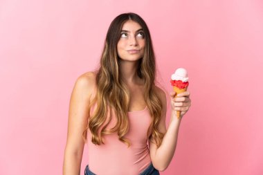 Kornet dondurması olan beyaz bir kadın pembe arka planda izole edilmiş ve yukarı bakıyor.