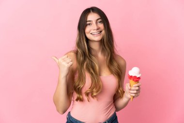 Kornet dondurması olan beyaz bir kadın pembe arka planda izole edilmiş bir şekilde bir ürün sunmak için kenarı işaret ediyor.