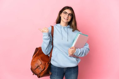 Pembe arka planda izole edilmiş genç bayan bir ürünü sunmak için kenarı işaret ediyor.