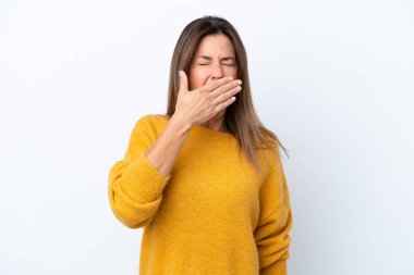 Beyaz arka planda izole edilmiş orta yaşlı beyaz bir kadın esniyor ve ağzını eliyle açık tutuyor.