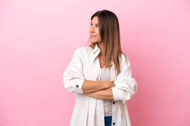 Orta yaşlı beyaz kadın pembe arka planda izole edilmiş, kollarını kavuşturuyor.