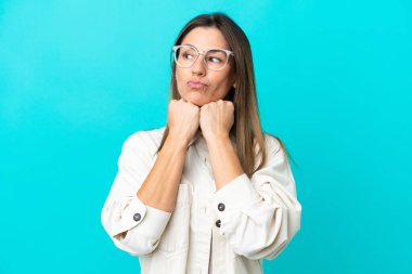 Mavi arka planda soyutlanmış, gözlüklü ve yorgun orta yaşlı beyaz kadın.