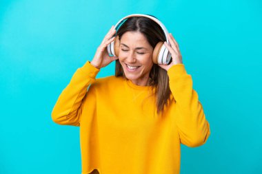 Orta yaşlı beyaz kadın mavi arka planda izole edilmiş müzik dinliyor.