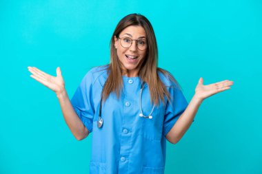 Orta yaşlı kadın cerrah. Mavi arka planda izole edilmiş. Yüzünde şok ifadesi var.