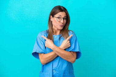 Mavi arka planda izole edilmiş orta yaşlı cerrah kadın, yan taraftakilerin şüphelerine işaret ediyor.