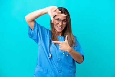 Orta yaşlı cerrah kadın, mavi arka planda izole edilmiş, yüzüne odaklanmış. Çerçeve sembolü