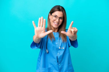 Mavi arka planda izole edilmiş orta yaşlı cerrah kadın parmaklarıyla yediyi sayıyor