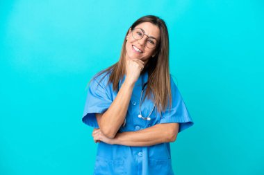 Mavi arka planda, gözlüklü ve gülümseyen orta yaşlı cerrah kadın.