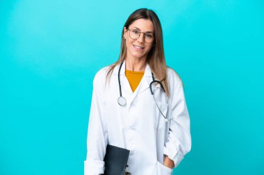 Mavi arka planda izole edilmiş orta yaşlı bir kadın doktor önlüğü giyiyor ve elinde bir klasör tutuyor.