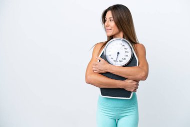 Orta yaşlı beyaz kadın, beyaz arka planda izole edilmiş, tartı makinesi olan ve yan bakan.